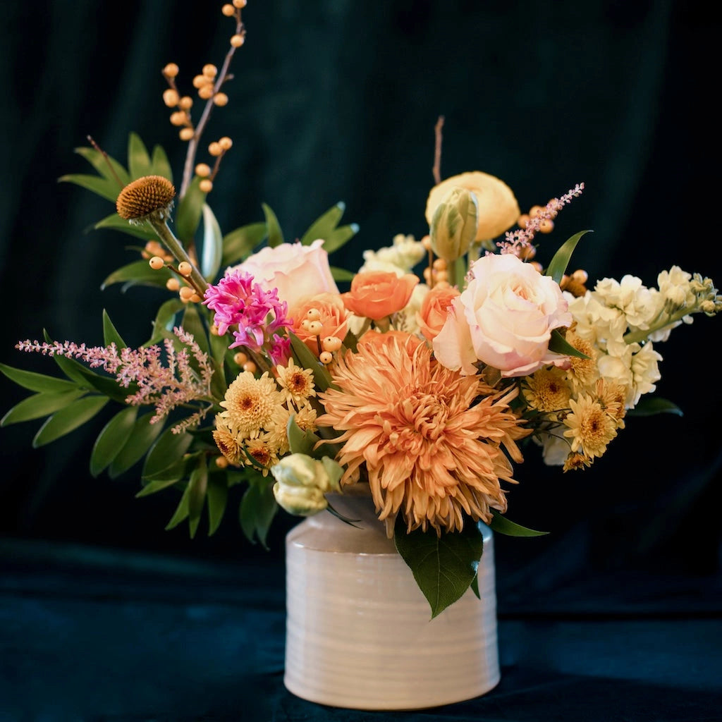 Campanula Design's "Mandarin" floral arrangement features a palette of soft pinks, buttery yellows, peach, and shades of orange designed in a ceramic vessel. 