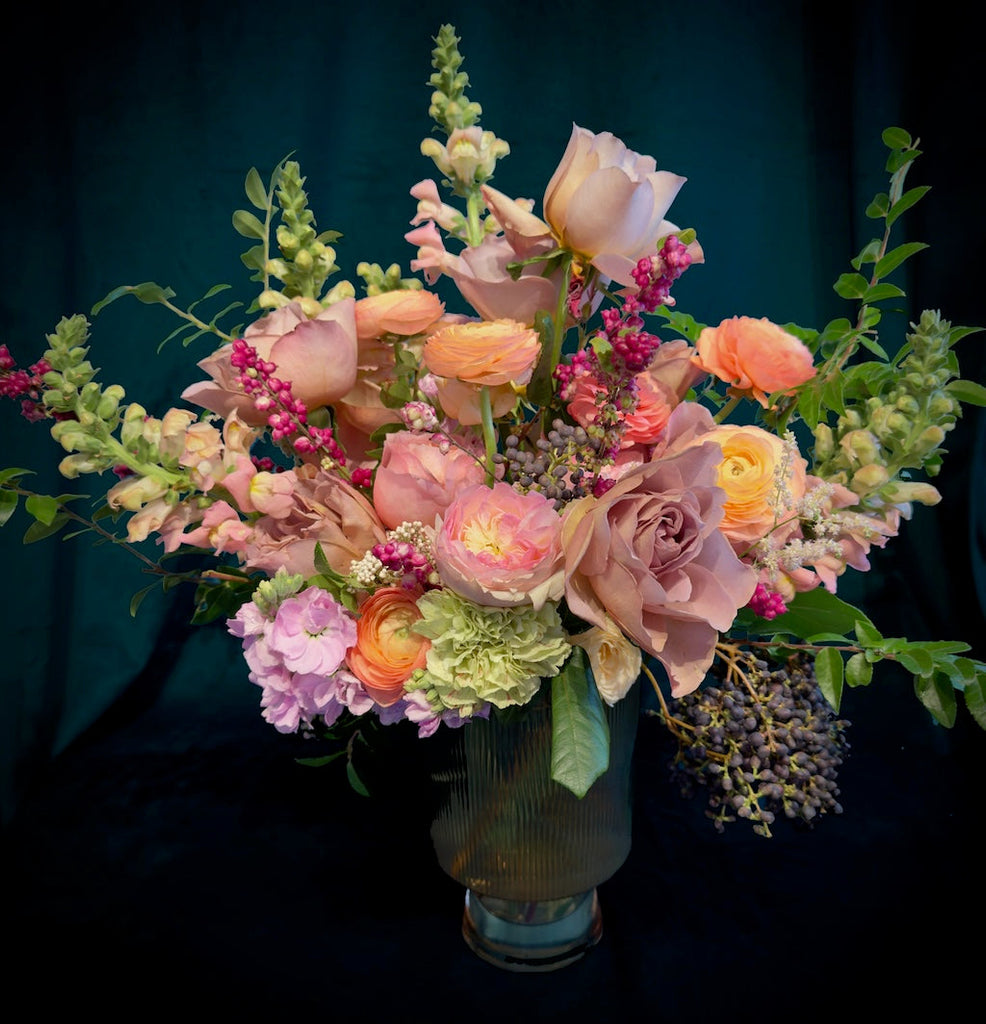 In colorful shades of pink, yellow, and orange offset by vibrant and lush greens, this stunning floral is designed in a glass pedestal vase. This flower arrangement is perfect for Valentine's Day for Seattle area delivery.