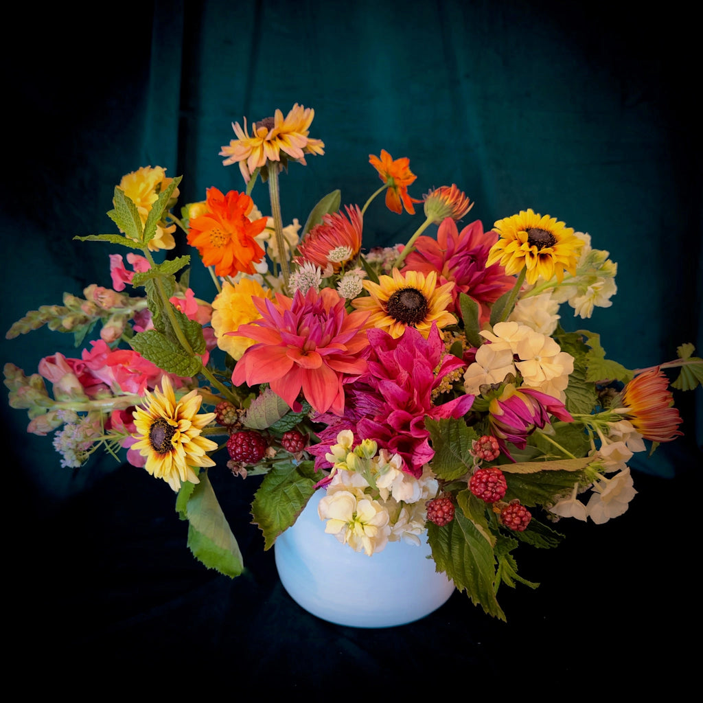 Our flower arrangement "Sunset" features vibrant oranges, pinks, and yellows  designed in a ceramic vase.